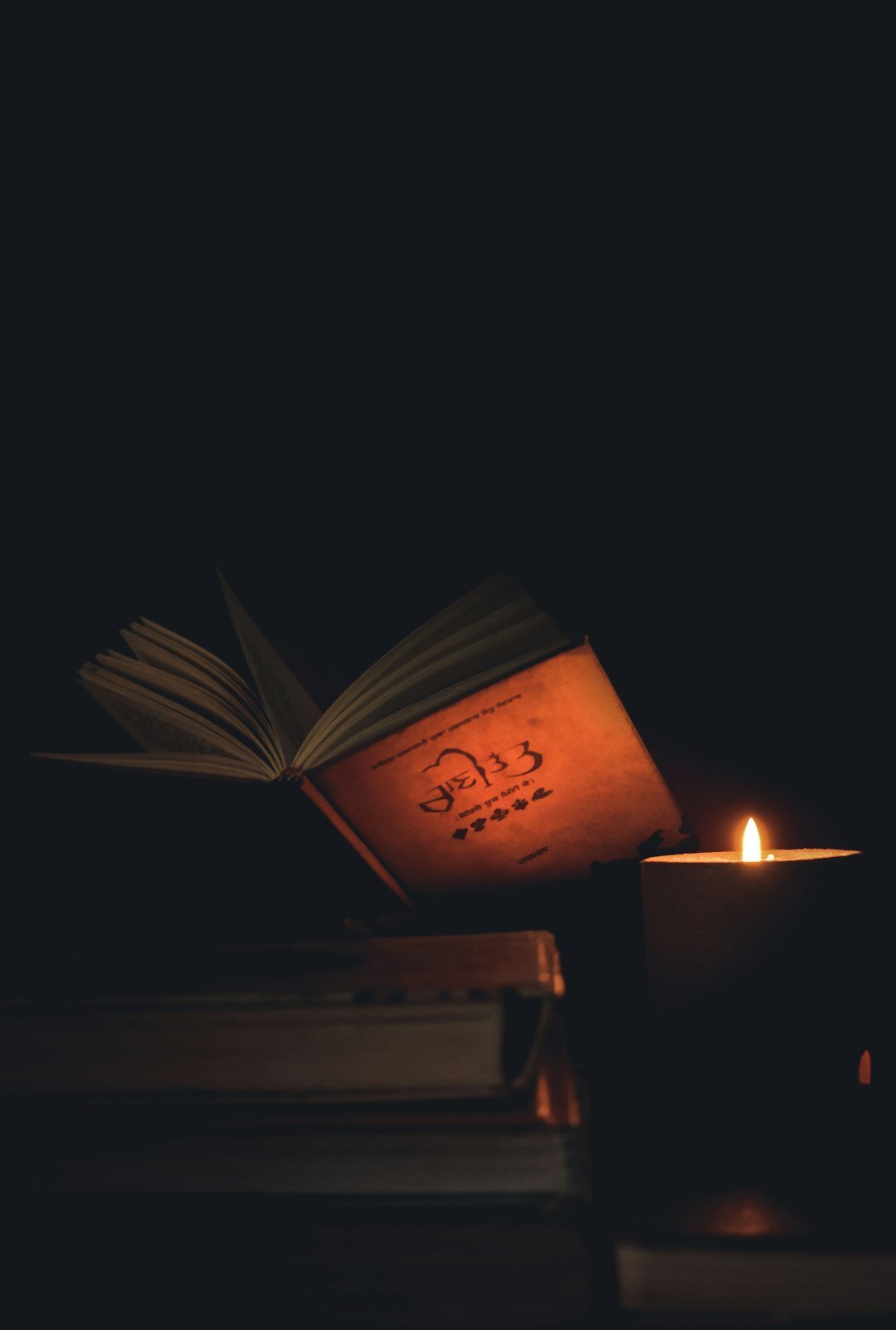 Stack of old leather bound books beside a burning candle